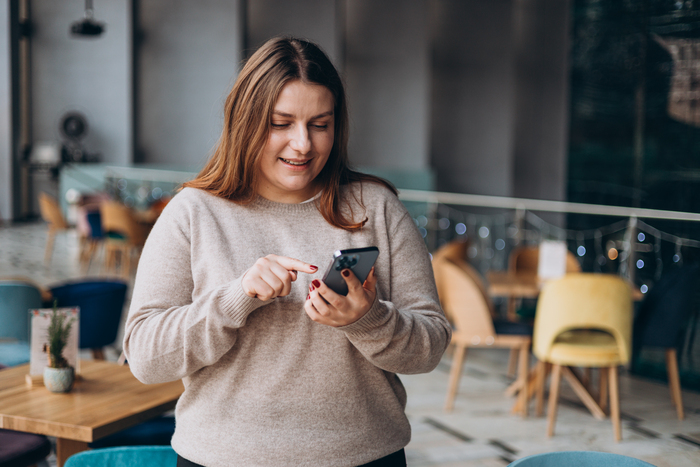 Woman smiling while looking at her smartphone in a brightly lit room